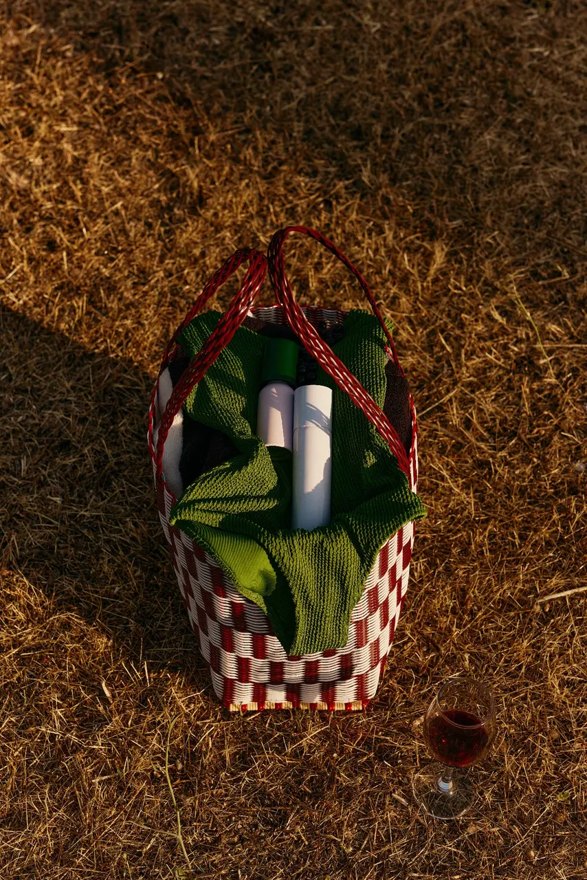 Woven bag holding folded fabric and travel containers on dry grass